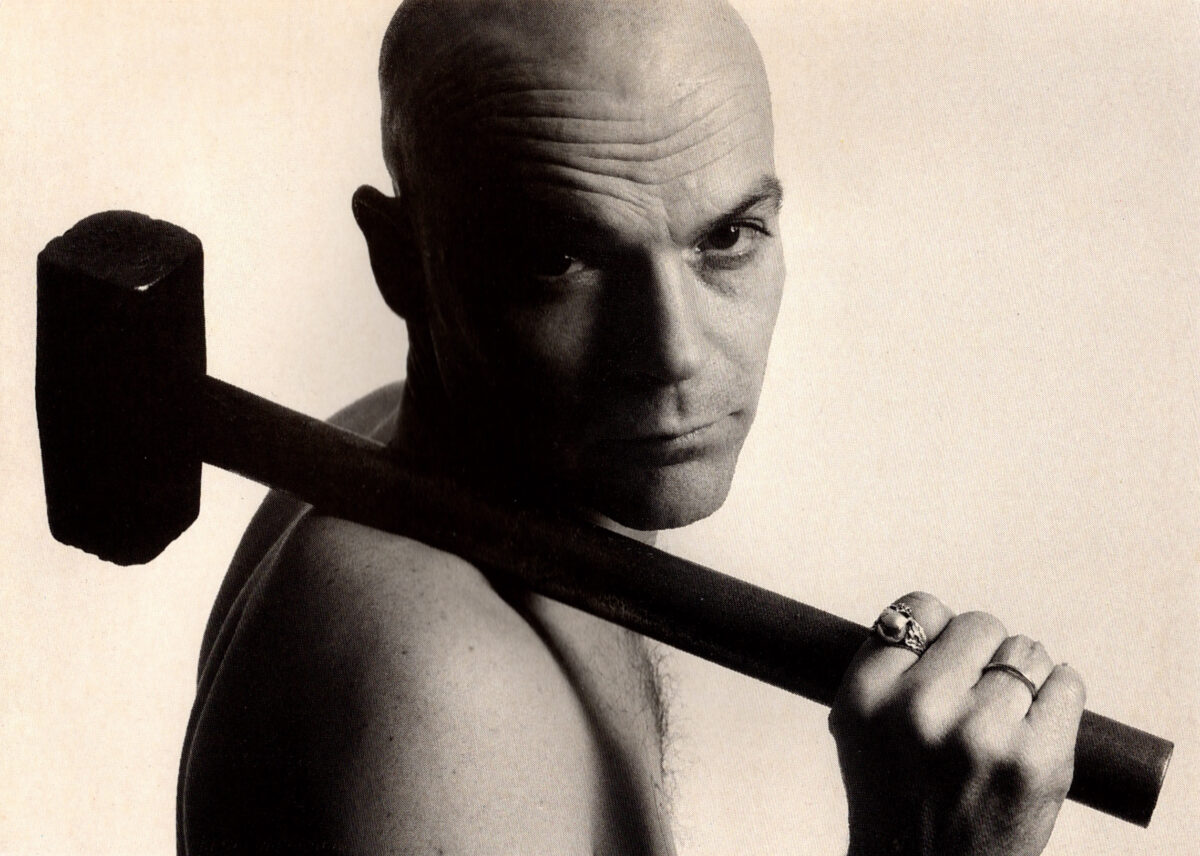 Schwarz-Weiß Porträt eines kahlen Mannes mit einem Hammer über der Schulter