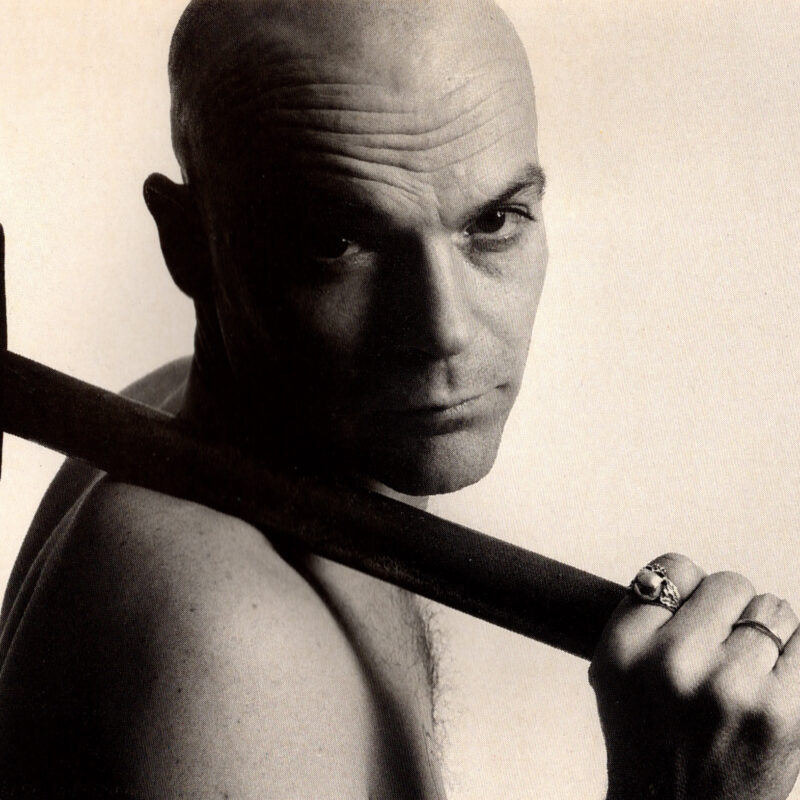 Schwarz-Weiß Porträt eines kahlen Mannes mit einem Hammer über der Schulter