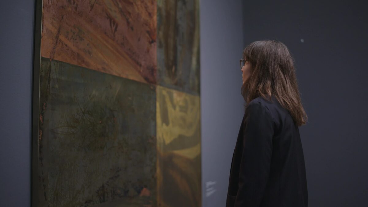 Eine Frau mit braunen Haaren betrachtet ein Kunstwerk (Robert Rauschenberg "Jungle Watch" aus der Serie "Borealis")