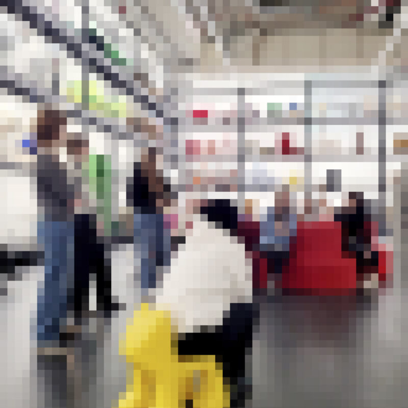 Mehrere Personen in einem modernen Raum mit hohen Regalen und einer gelben Hundeskulptur im Vordergrund.